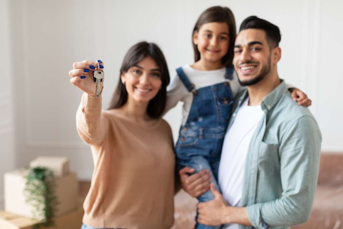 Positive family of three showing house key, standing in living room of new home,