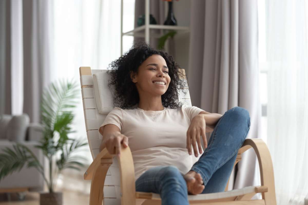 Smiling calm young black woman relaxing on comfortable wooden rocking chair